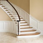 Curved staircase with paneled wainscoting, wood balusters, and over-the-post railing.