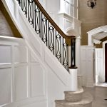 Curved stair with custom wrought iron balusters. Stair features panel detailing and stone treads and risers.